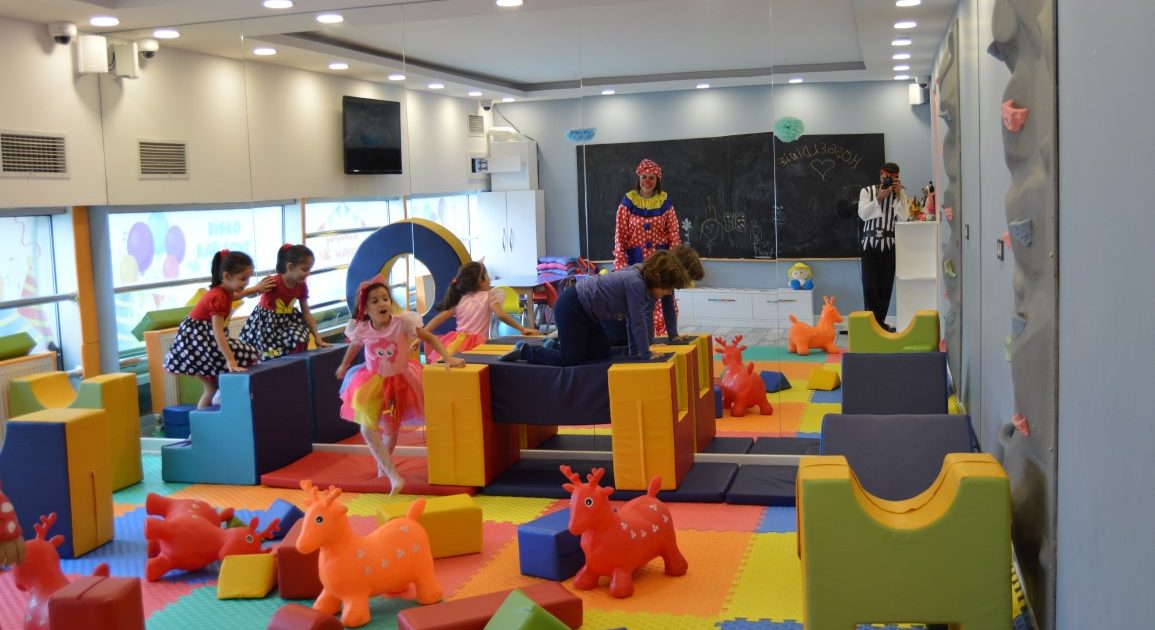 Children playing with a clown in the play area, with soft blocks, bouncy toys and a climbing wall