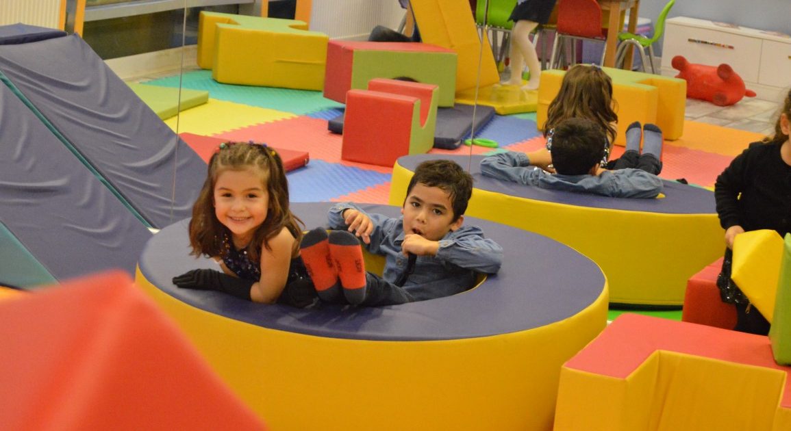 Smiling children lying inside round soft play blocks