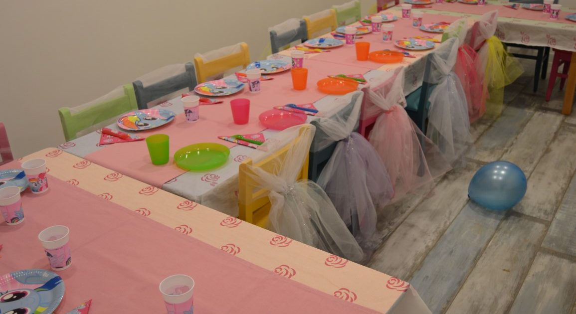 Renkli tabak ve bardaklarla kurulmuş, sandalyeleri tülle süslenmiş çocuk parti masası