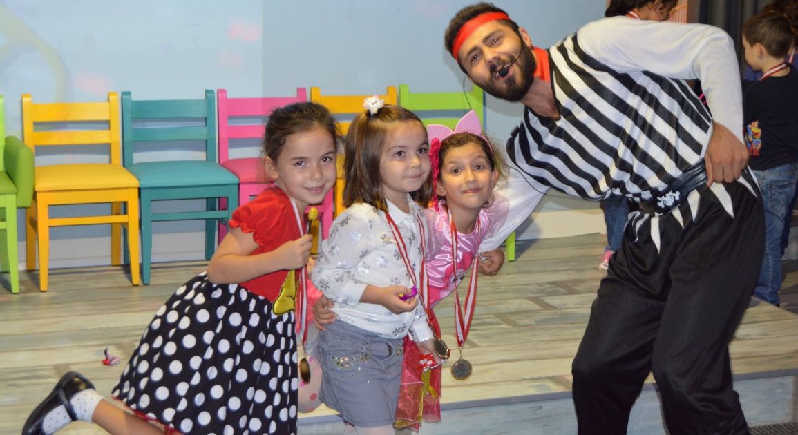 Three girls posing with medals around their necks beside an entertainer in a striped shirt