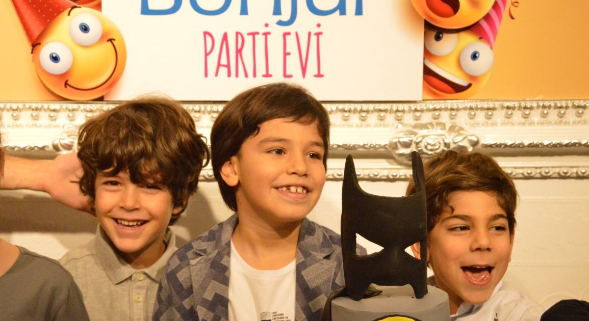 Three boys laughing in front of the “Bonjur Parti Evi” sign