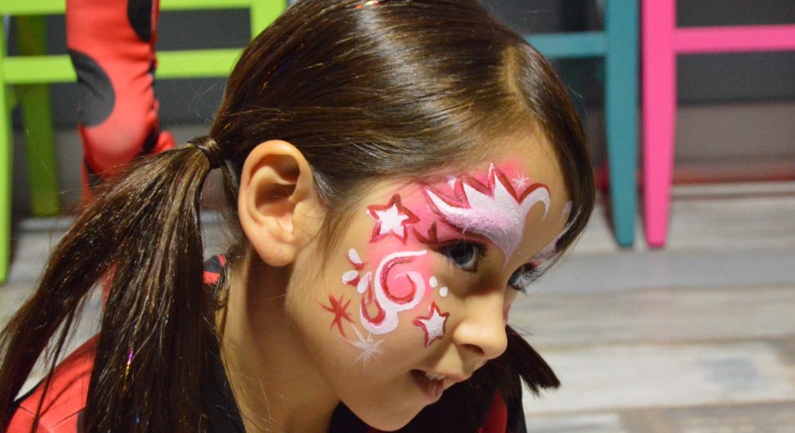 A child with a face painting of pink and white stars and swirls